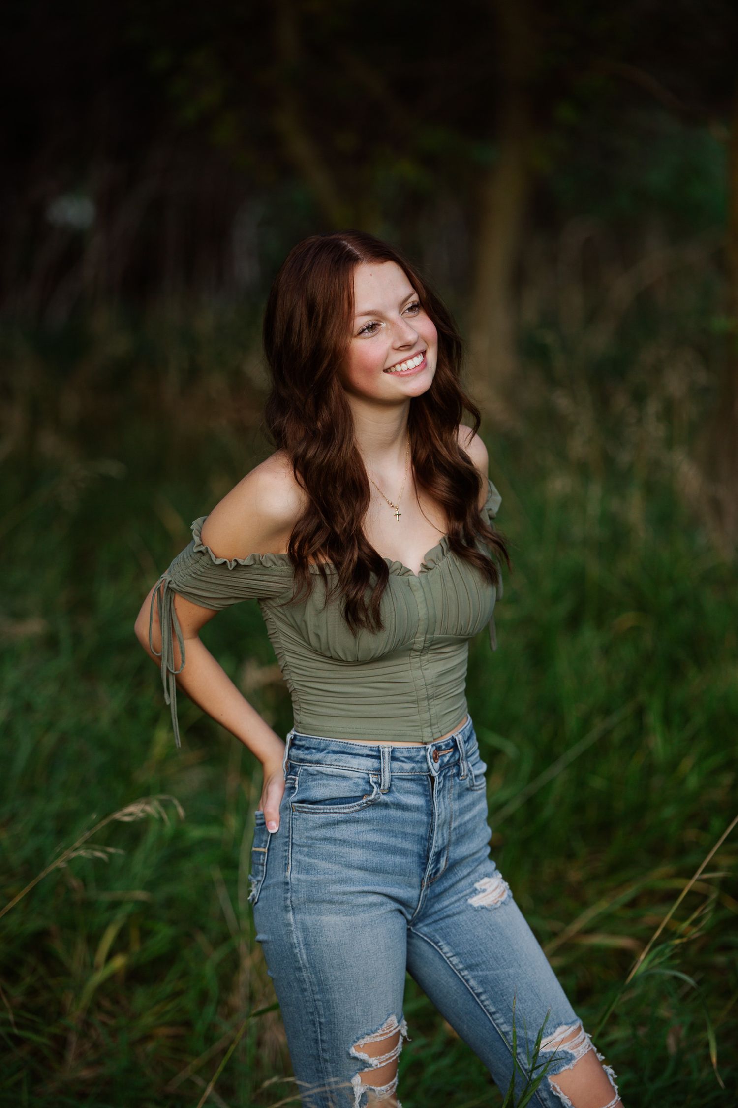 A woman in a green dress poses on grass during an outdoor portrait photography session.