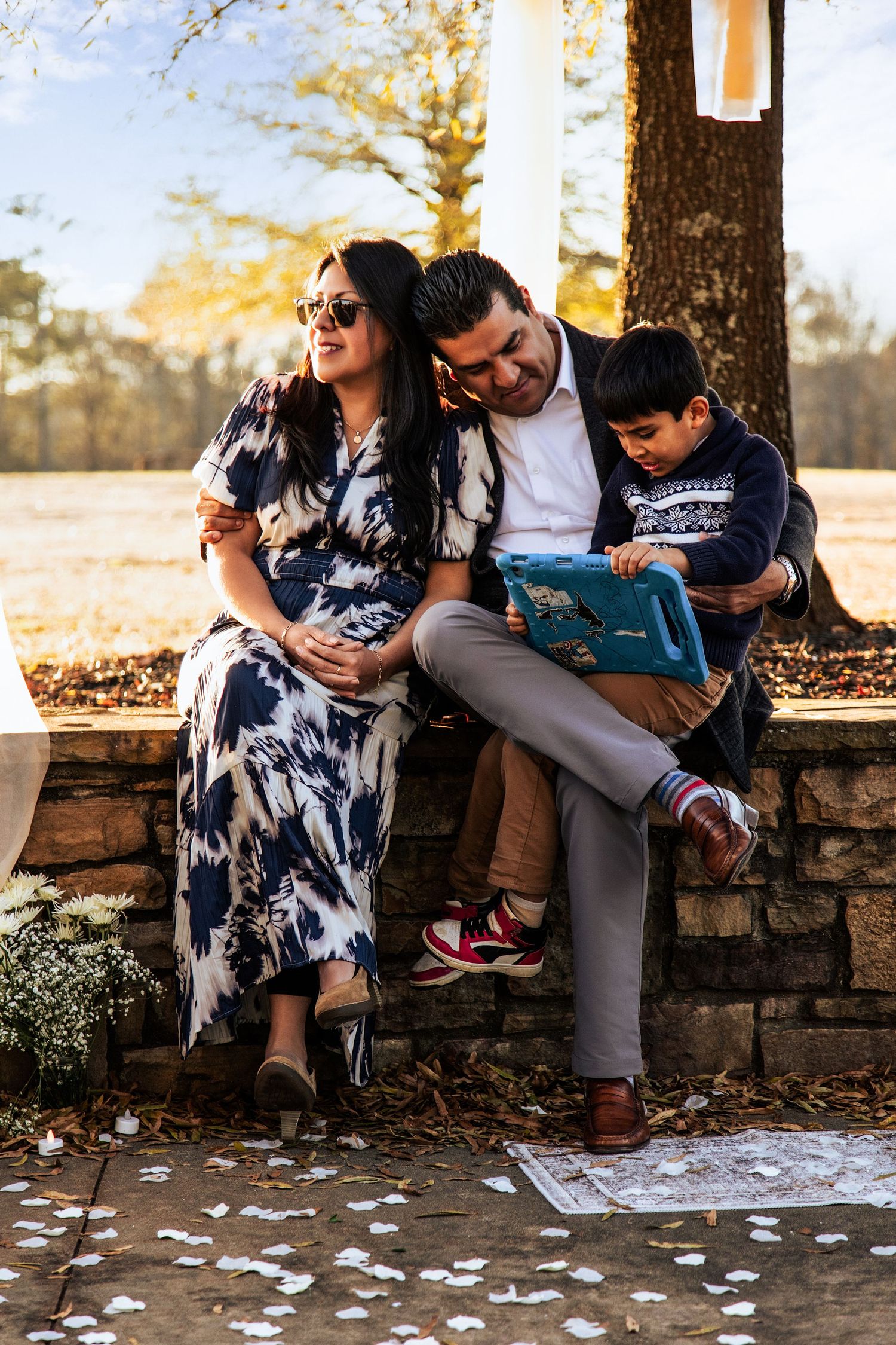 Family sitting together on stone wall during autumn with scattered leaves on ground.