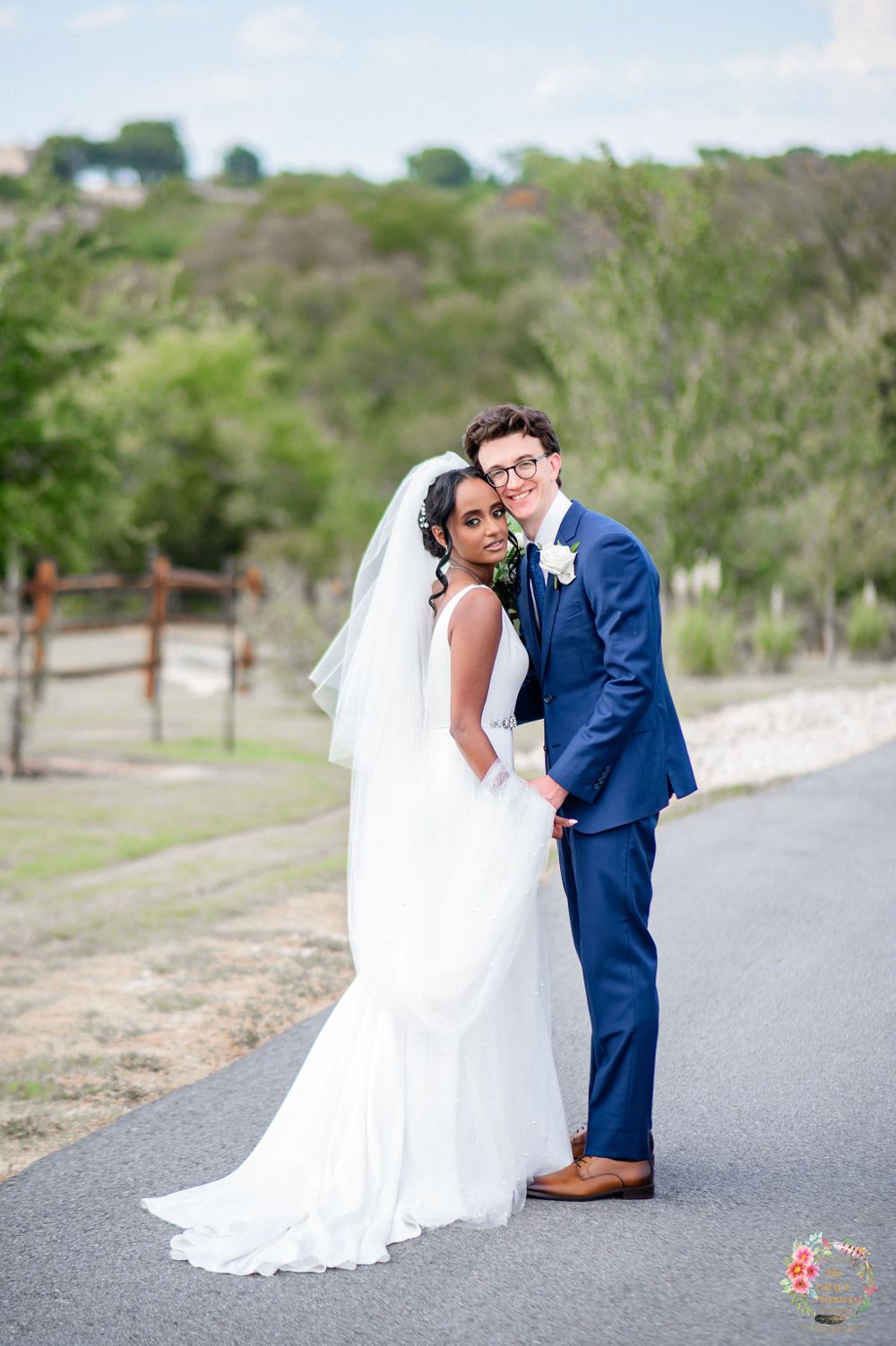 Newlyweds share a romantic moment on a paved path with greenery in the background.