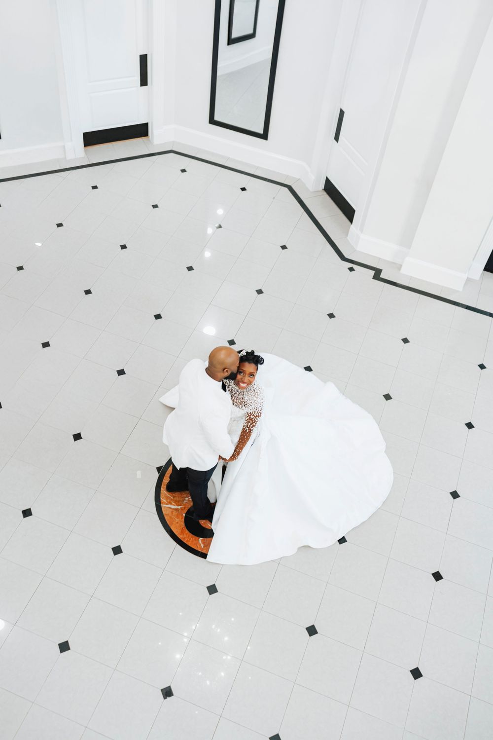 Aerial view of a couple dancing on elegant white and black checkered floor in formal wedding attire.