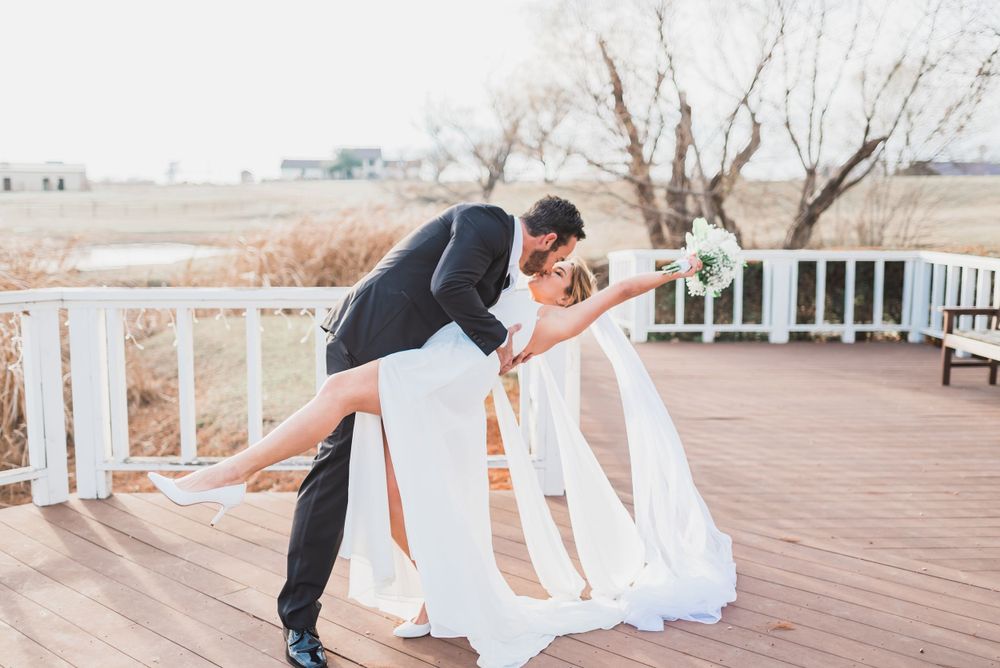 Romantic dip pose between bride and groom on outdoor deck during wedding photoshoot.
