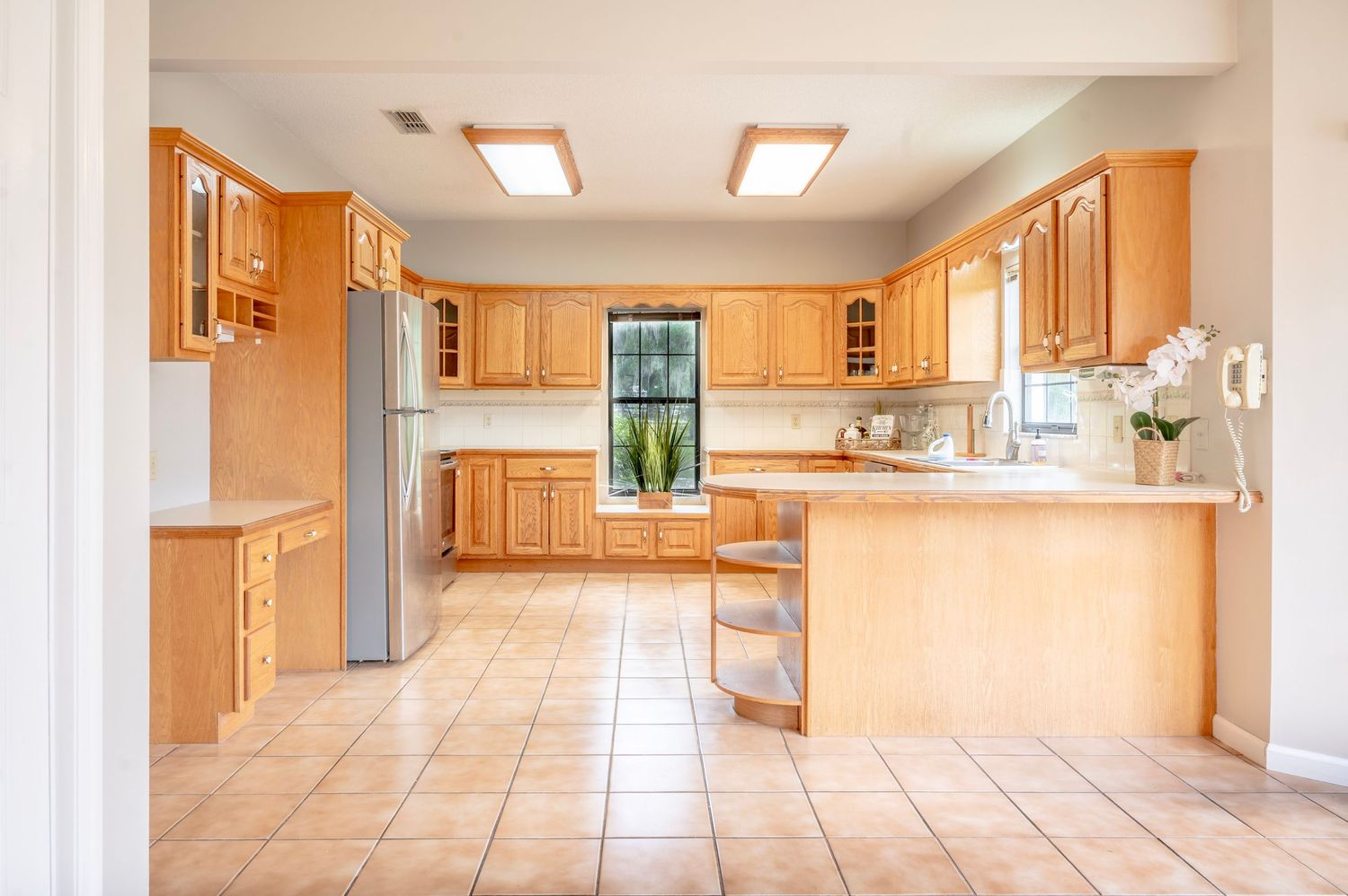 Large open kitchen with honey oak cabinets, tiled floors, and fluorescent lighting extends down a long hallway.
