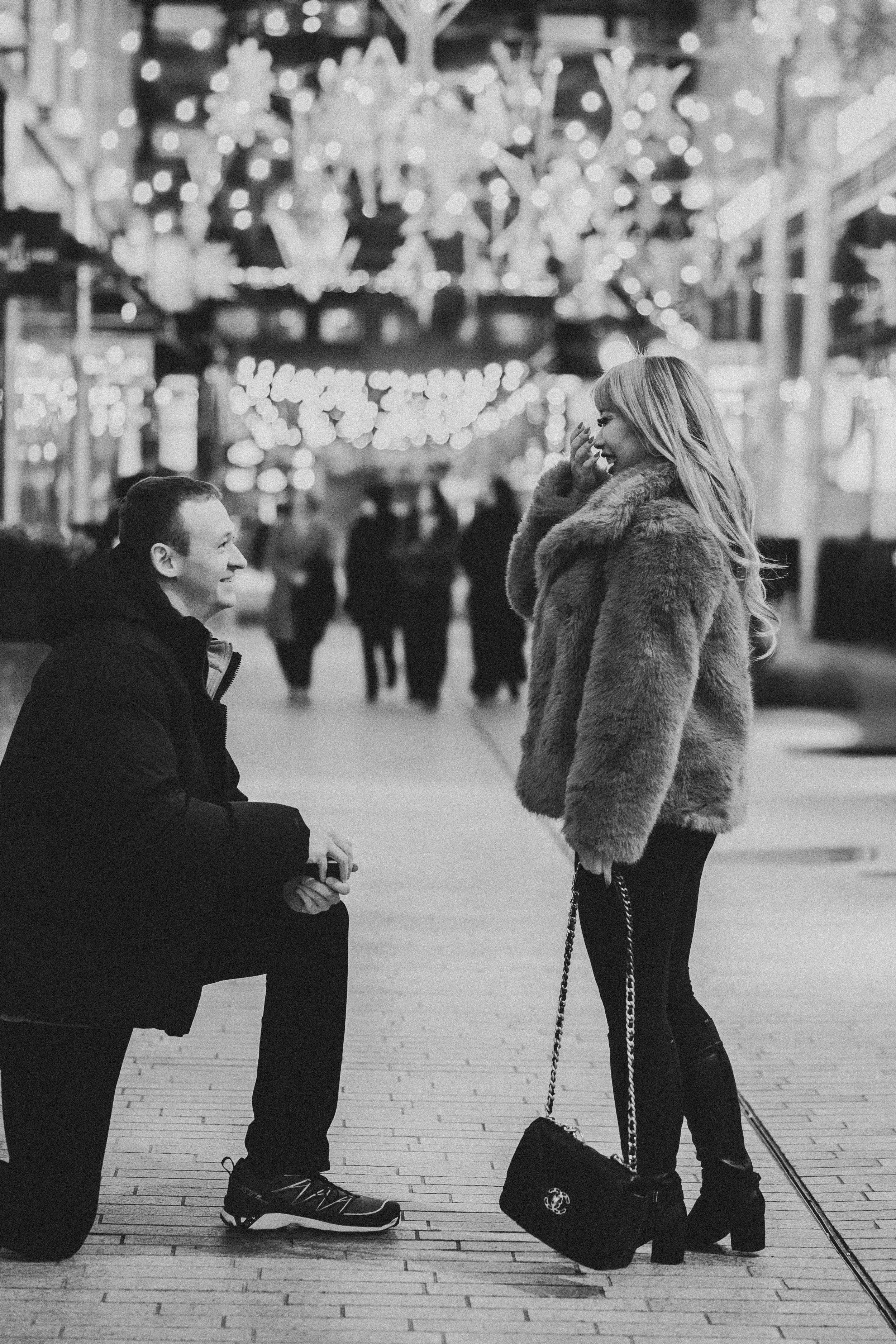 A black and white photo showing a man down on knee proposing to his love at the CityCenterDC, a great winter dc proposal spot
