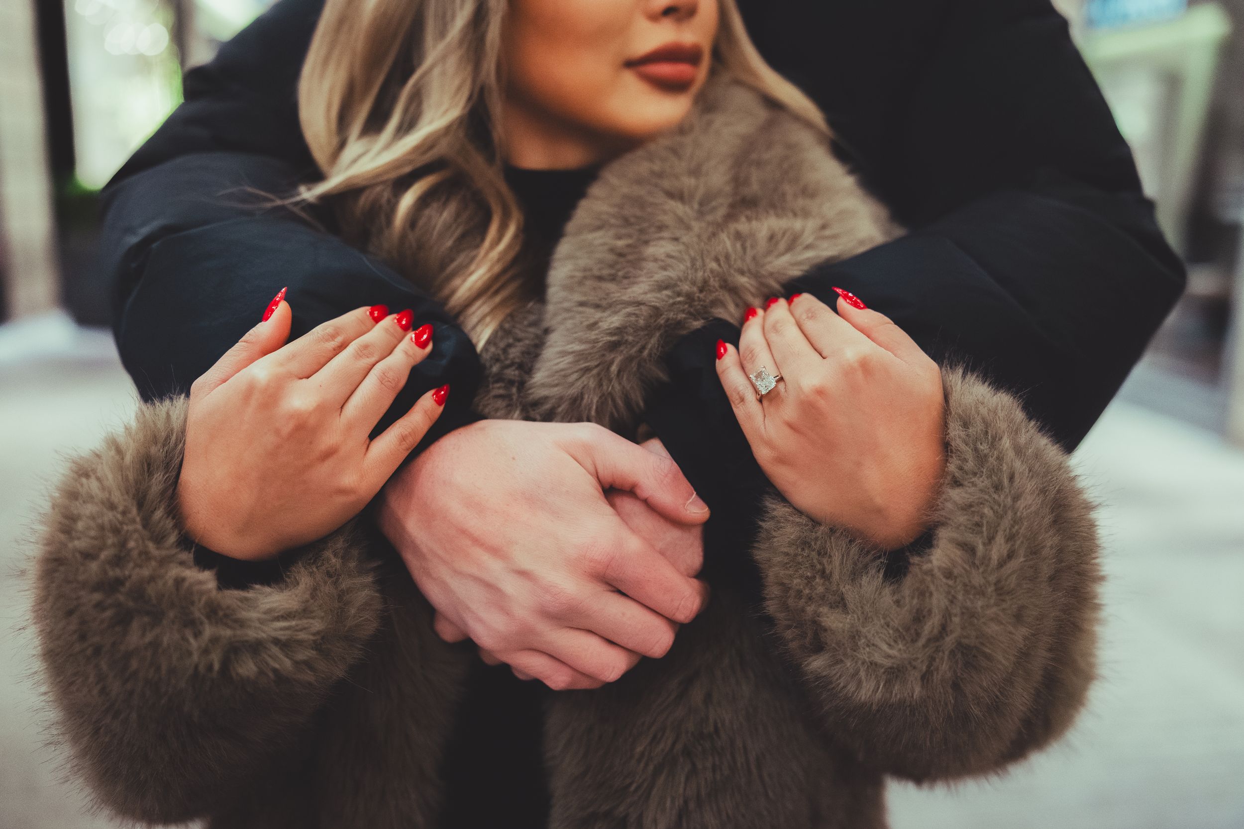 Close-up detail of hands and a new engagement ring against a blurred background.