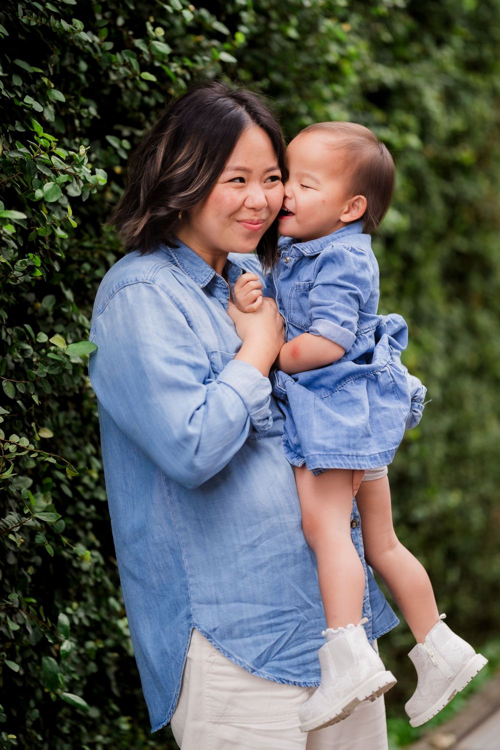 A tender moment captured outdoors with coordinating denim outfits against a green hedge background.