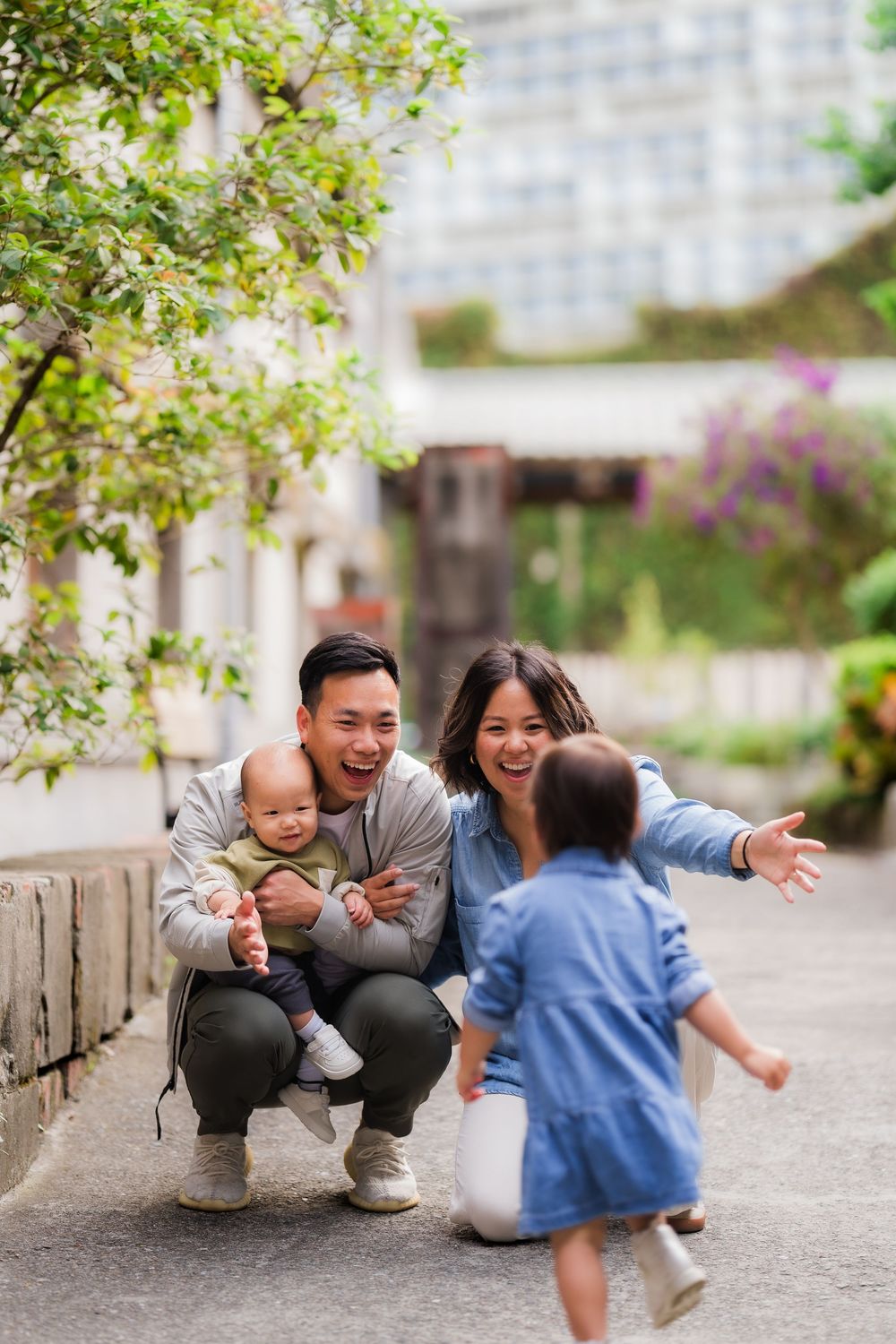 A family crouches down together on a stone path while sharing joyful moments in an outdoor garden setting.