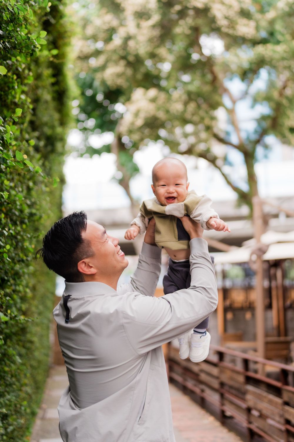 A heartwarming outdoor scene shows joyful interaction between parent and baby on a wooden walkway surrounded by greenery.