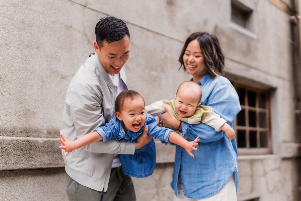 A family of four shares a joyful moment together while laughing and playing outdoors against a stone wall.