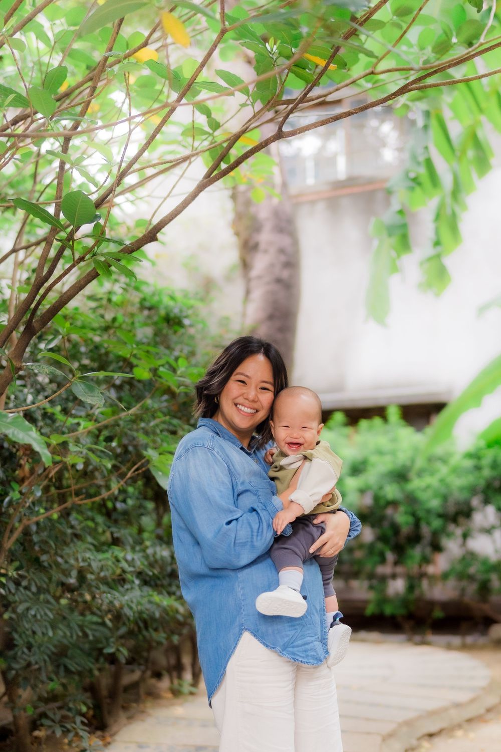 A pair shares joyful laughter together in a garden setting with green foliage in the background.