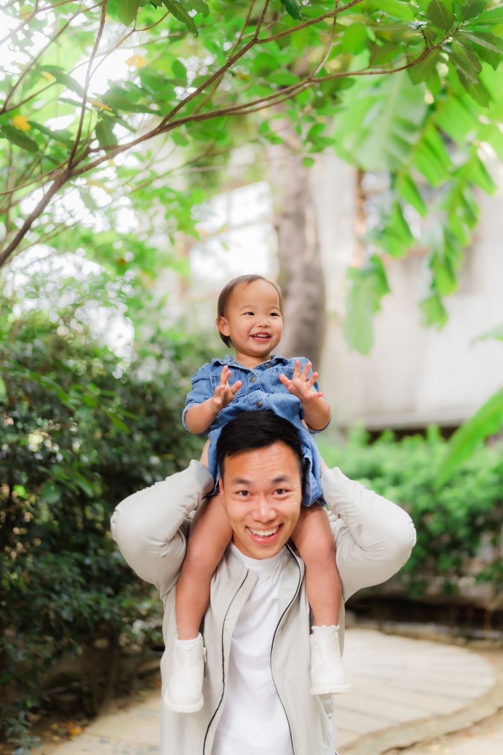 A joyful moment captured outdoors as a parent carries a laughing baby on their shoulders under green foliage.