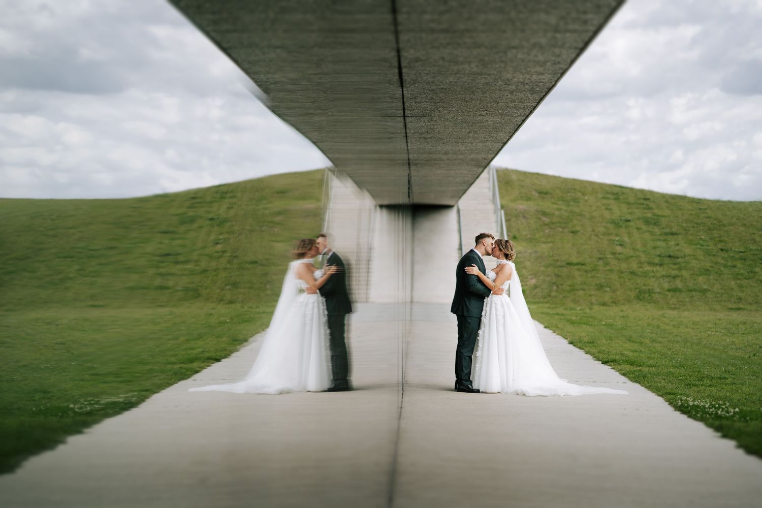 Elegant wedding couple poses under modern concrete architectural structure.