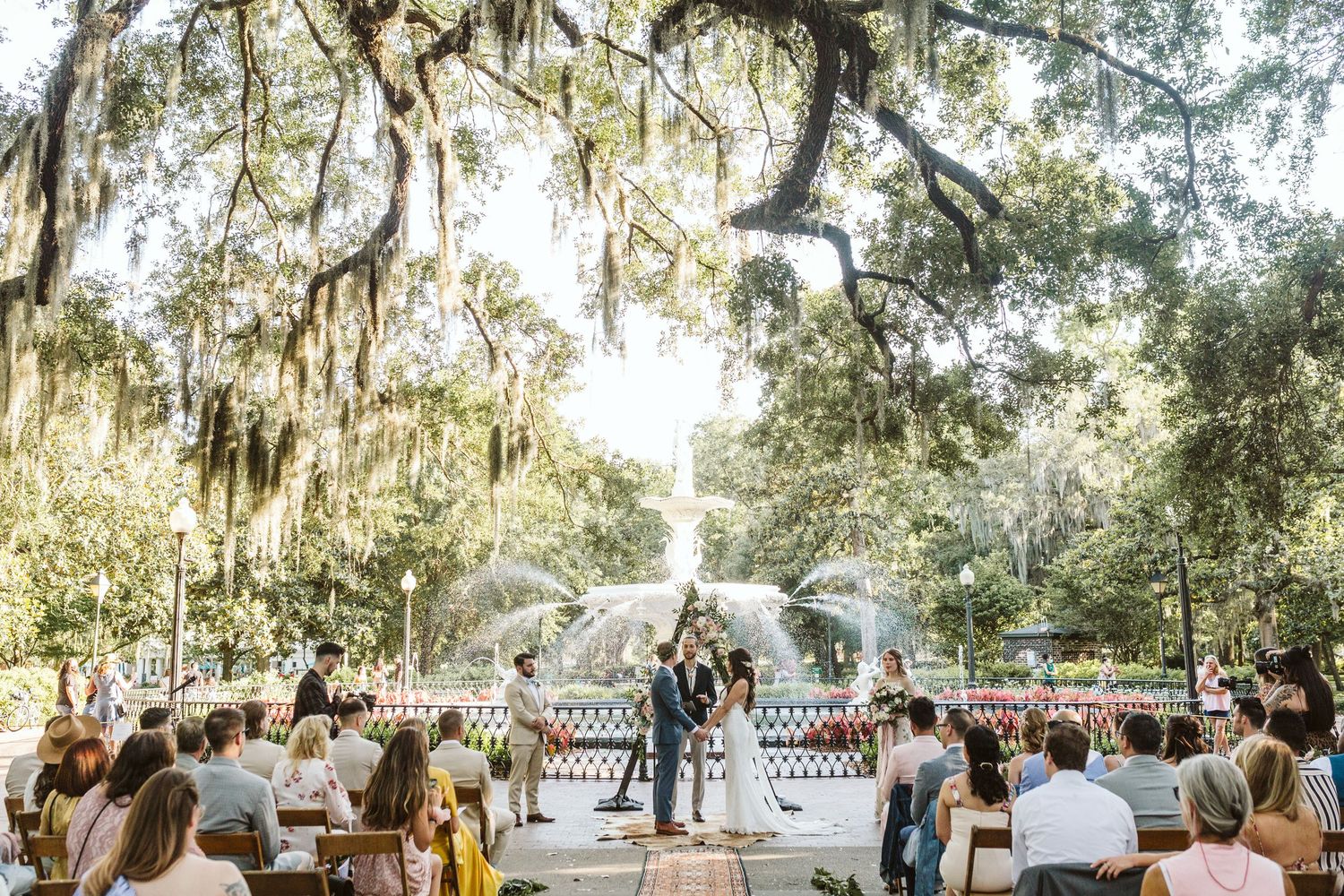 Wedding guests gather outdoors under moss-draped oak trees during a romantic garden ceremony in Florida.