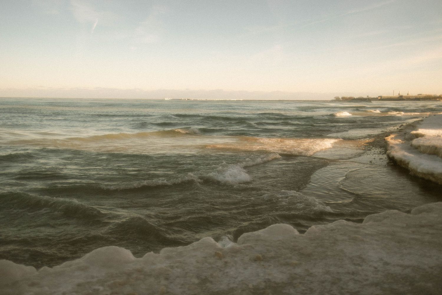 Dramatic seascape with dark stormy waves crashing against a rocky shoreline at sunset.