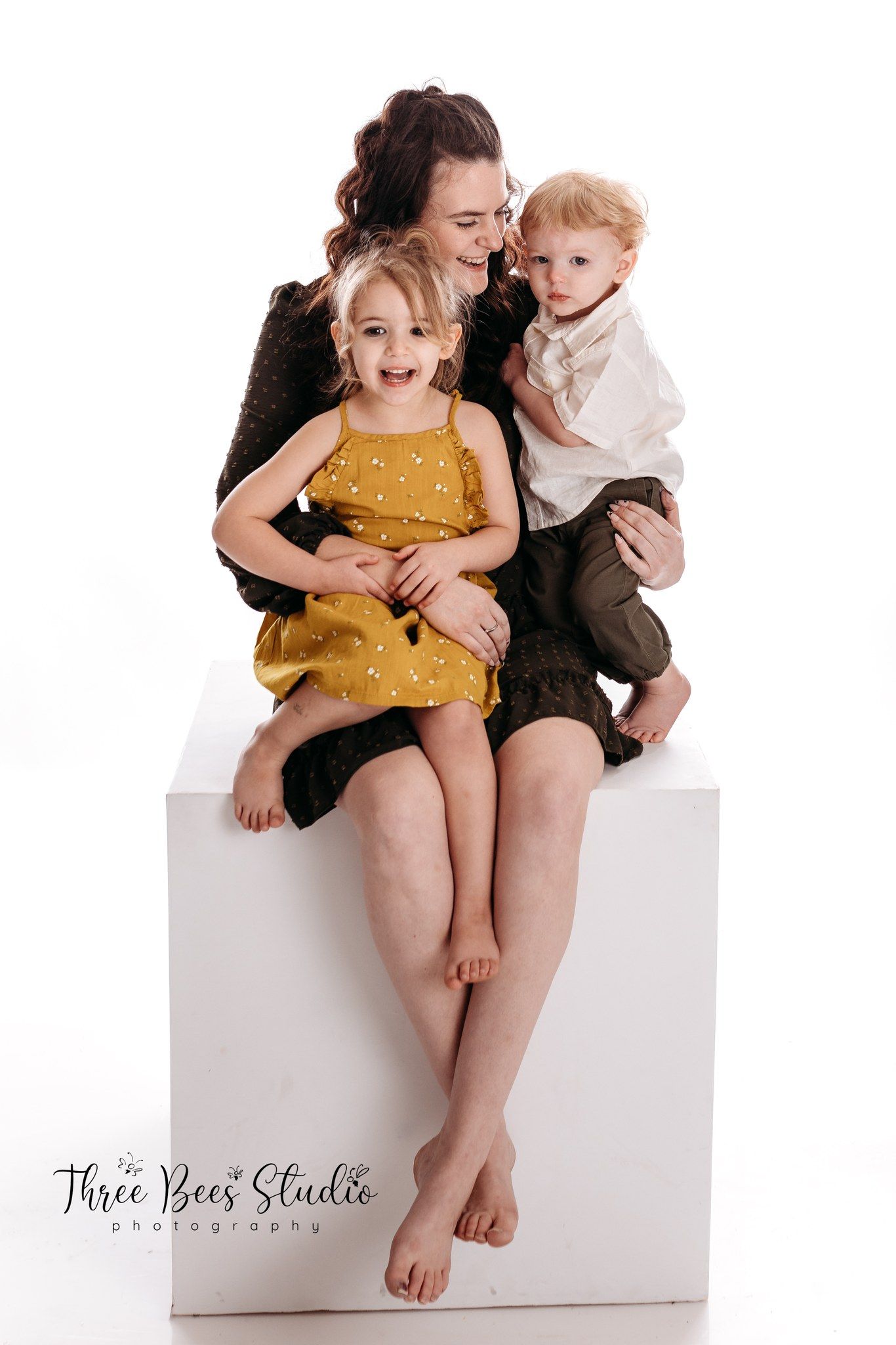 Studio portrait of a family sitting together on white backdrop with Three Bears Studio watermark.