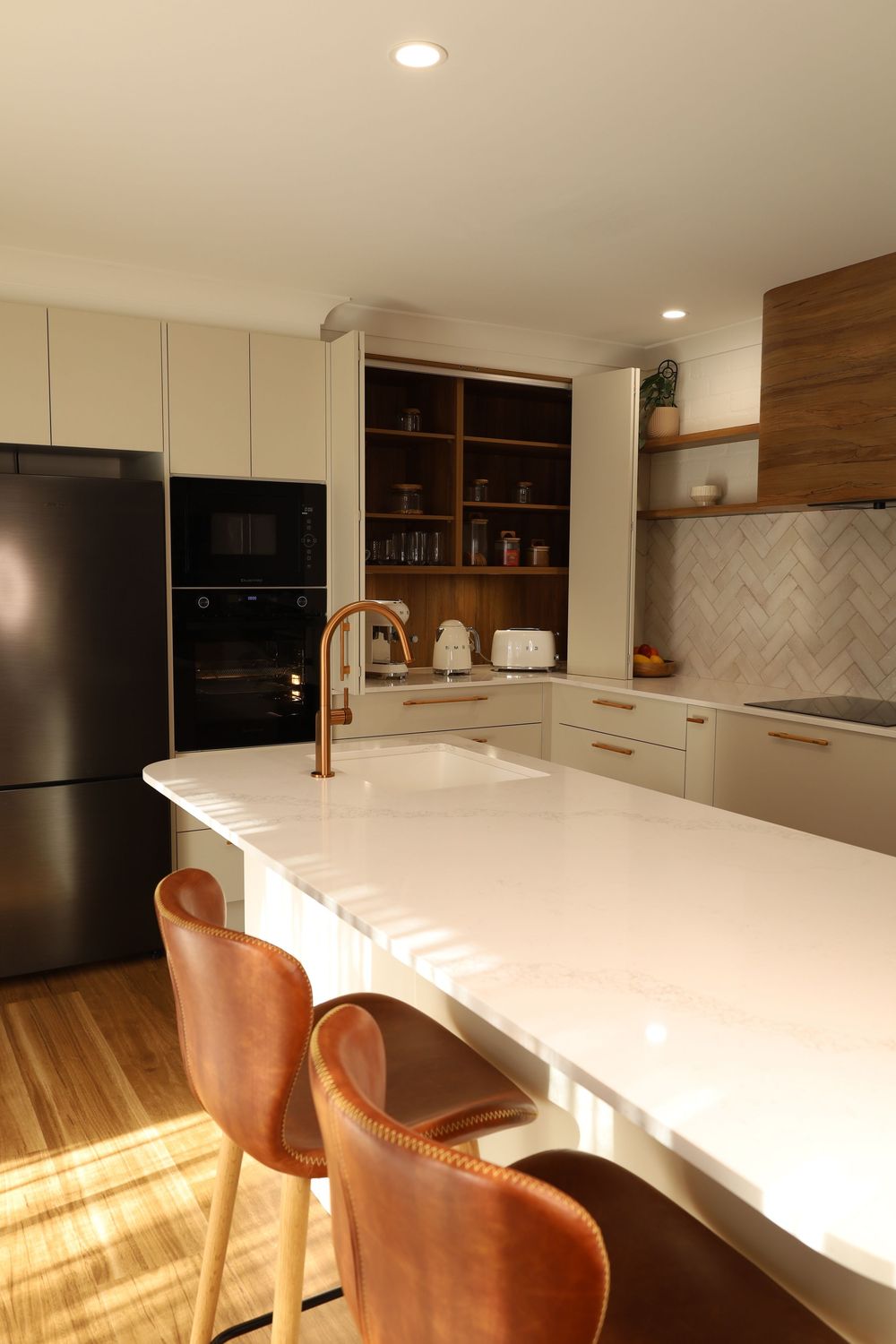Modern kitchen with white countertops, brown leather bar stools, and warm wood accents in natural lighting.