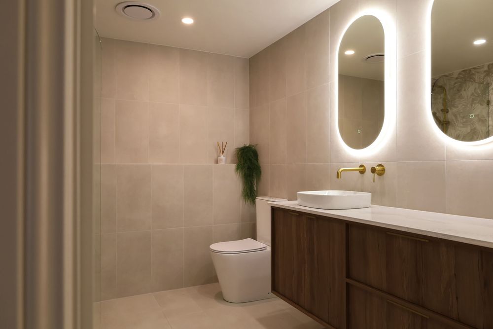 Modern bathroom interior with wooden vanity, round mirror, and neutral beige tones features minimalist design elements.