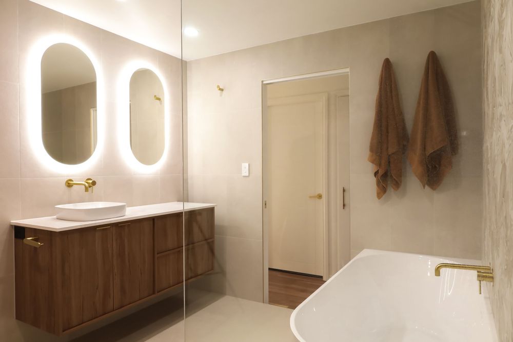 Modern bathroom interior with illuminated round mirrors, wooden cabinets, and sleek white walls and fixtures.