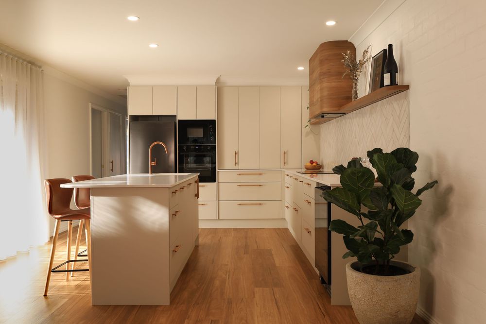 Modern white kitchen interior with recessed lighting, hardwood floors, and fiddle leaf fig plant in corner.