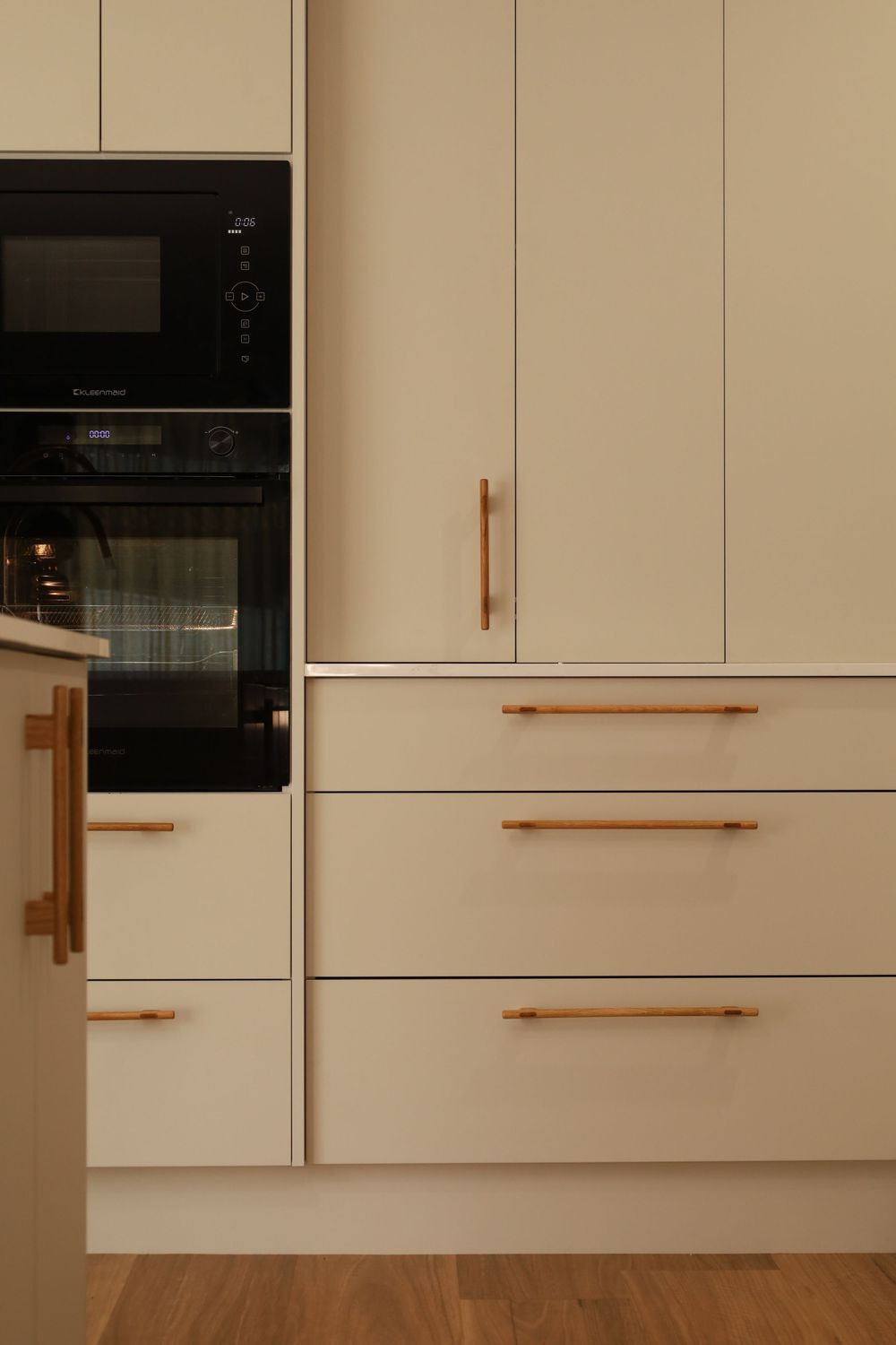 Contemporary beige kitchen cabinets with sleek copper handles and built-in black appliances.