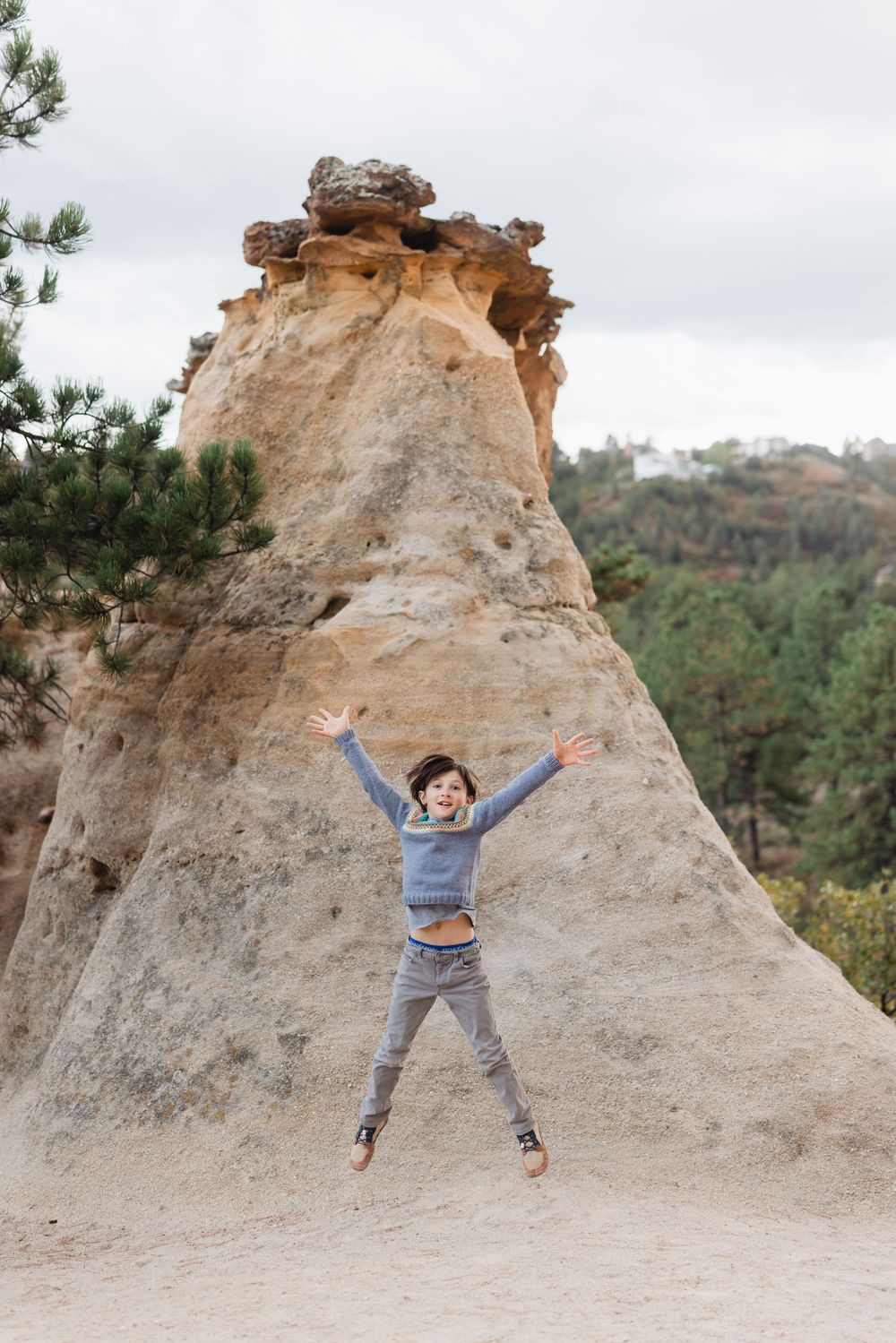 A person jumps joyfully in front of a tall limestone rock formation in a natural outdoor setting.
