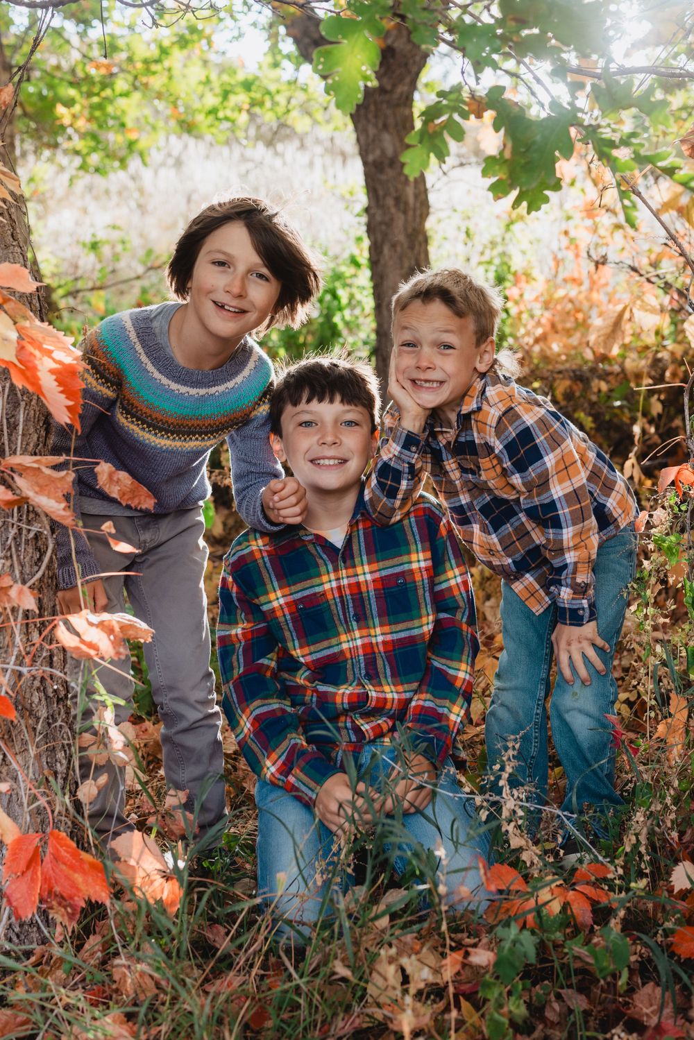 A family group poses together outdoors among autumn foliage and fallen leaves on a sunny day.