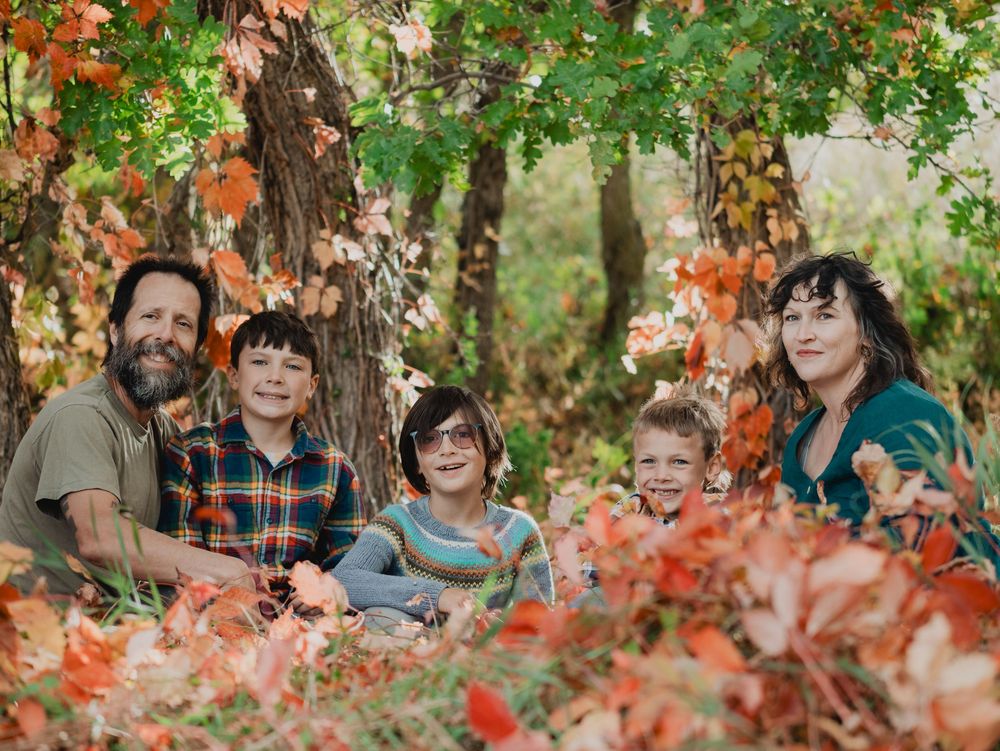 A group sits together outdoors among vibrant fall foliage and autumn leaves under tree branches.