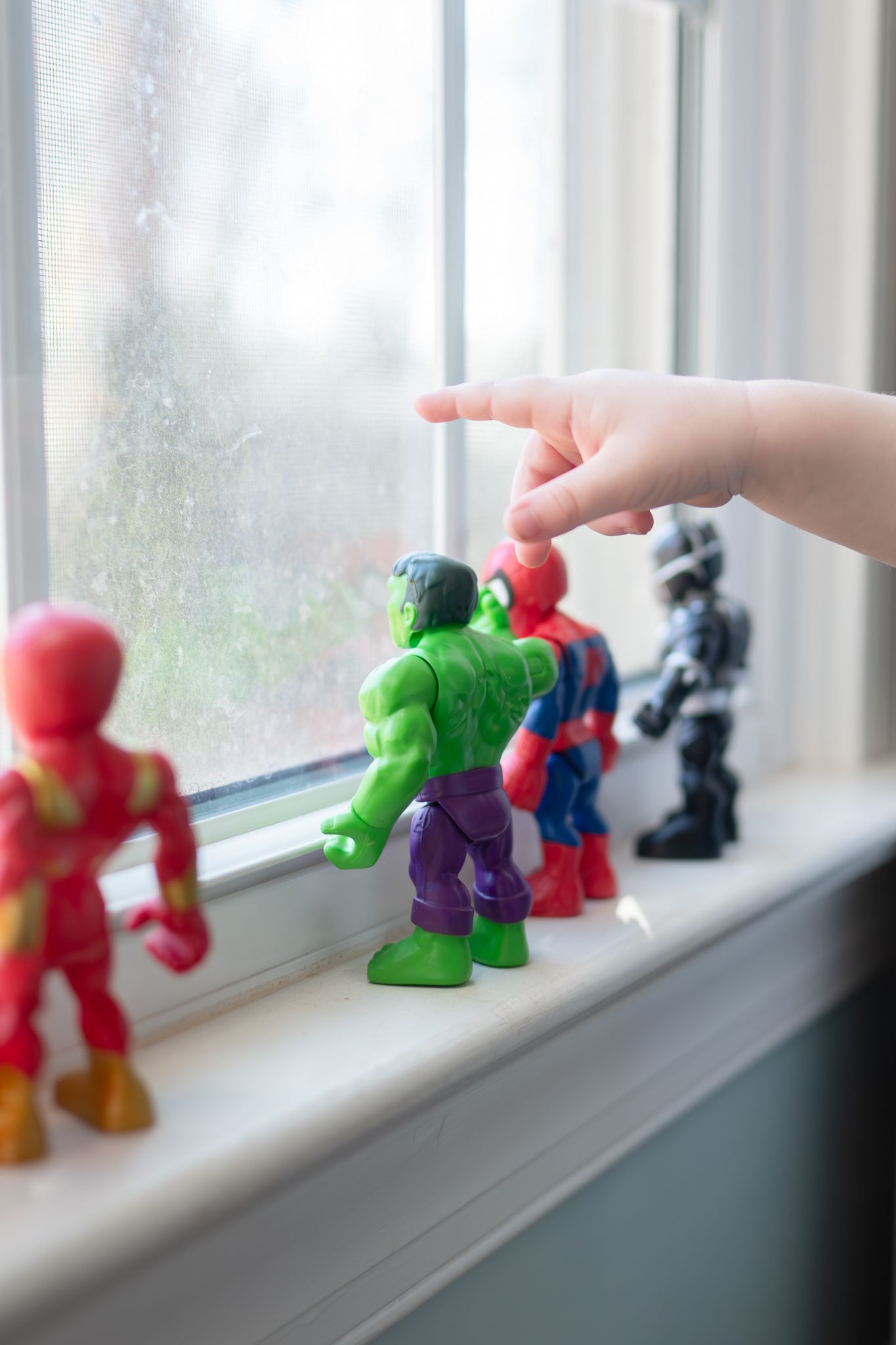 Colorful superhero action figures arranged in a line along a bright window sill.