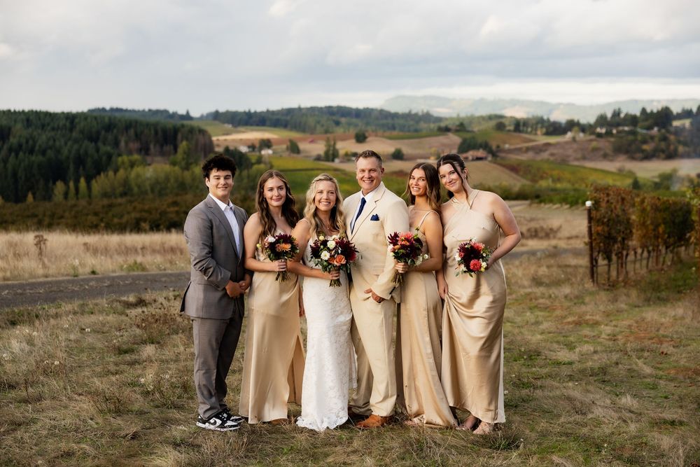 Wedding party in beige and white attire poses together on a scenic hillside during golden hour.