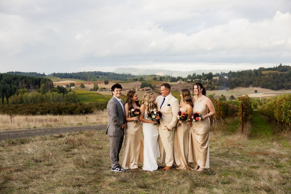 Wedding party in champagne colored dresses poses in front of scenic mountain landscape at sunset.