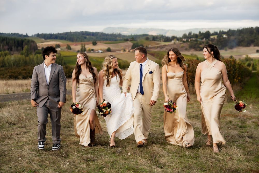 Wedding party walks along a scenic hilltop path with rolling countryside views in the background.