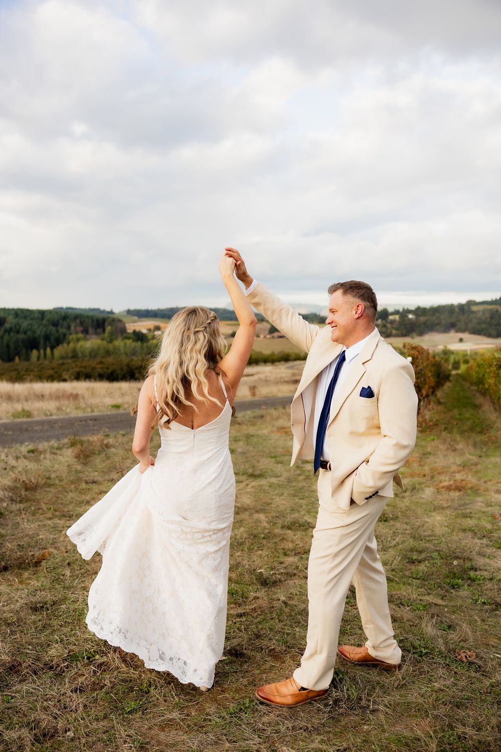 Wedding couple dances joyfully in a field with rolling hills in the background.