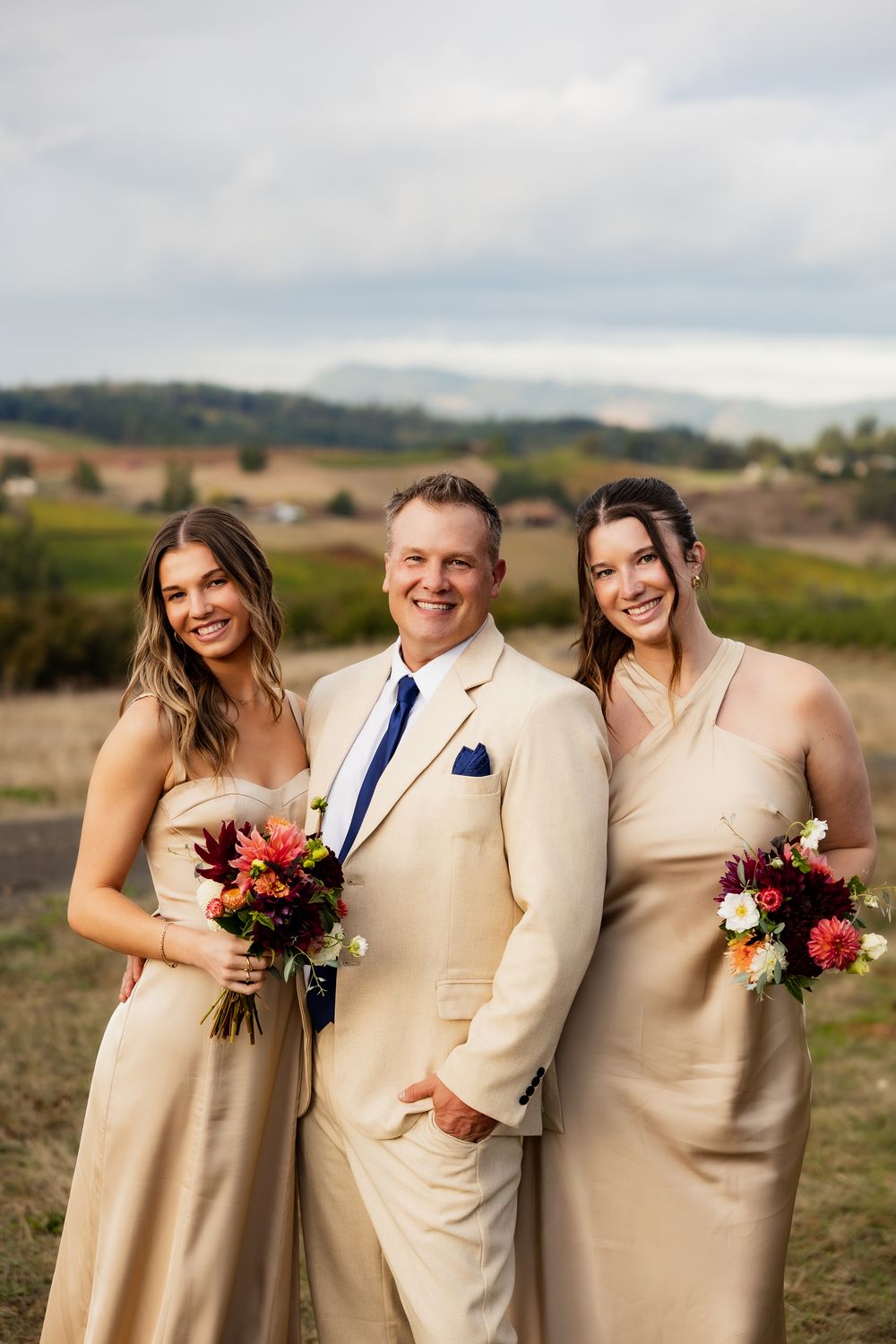 Wedding party in cream colored attire poses together in a rustic outdoor setting.
