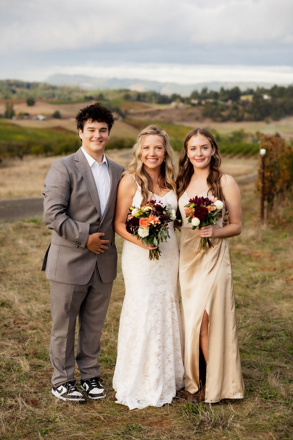 Wedding party poses together in an autumn field with bridesmaids in beige dresses and burgundy bouquets.