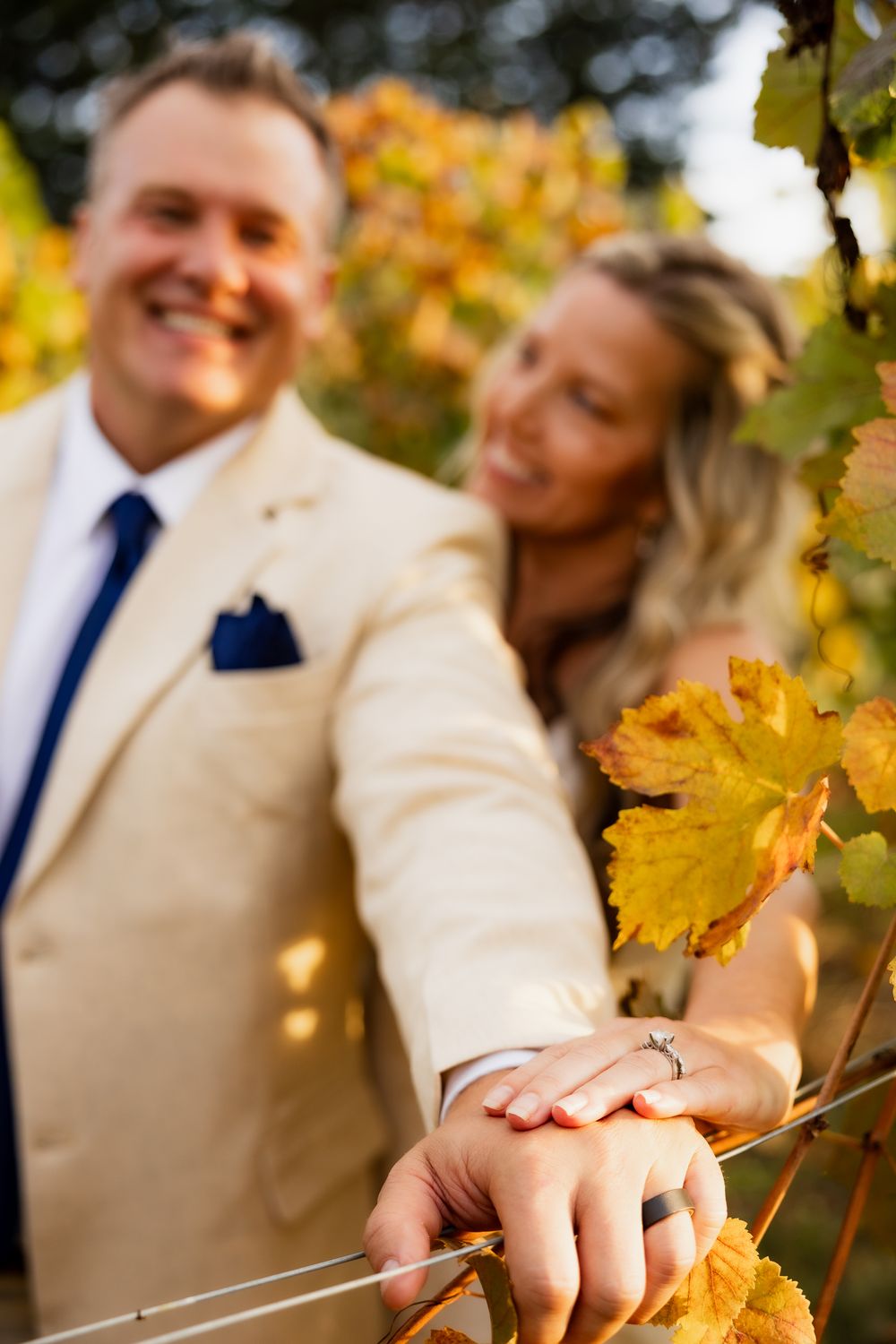 Close-up of hands touching autumn vineyard leaves during wedding photoshoot.