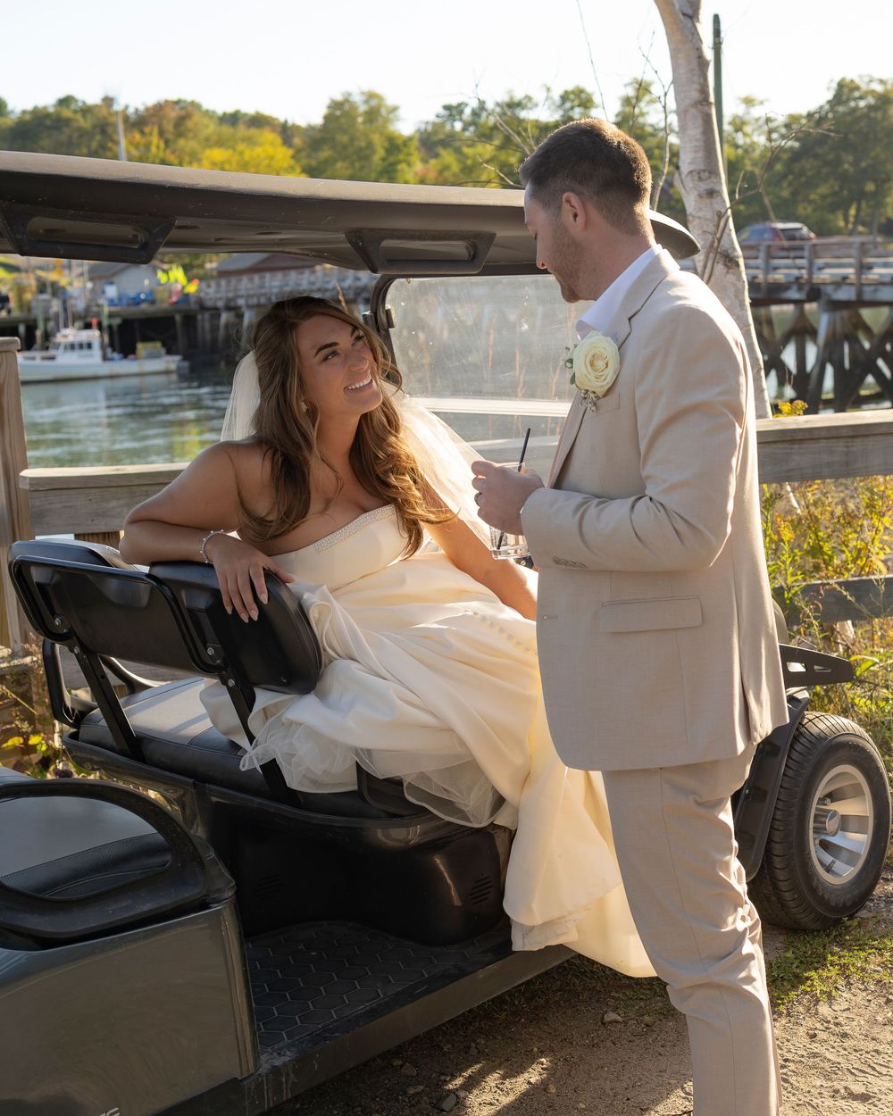 Newlyweds share a romantic moment in a golf cart at a marina during golden hour.