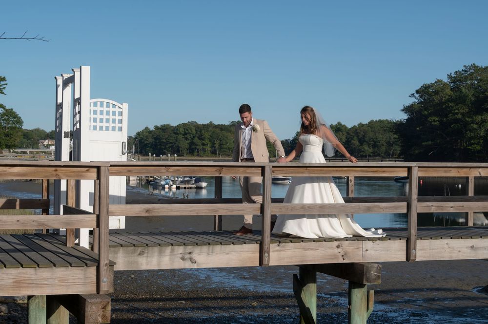 A couple sits together on a wooden dock overlooking a serene lake on a sunny summer day.