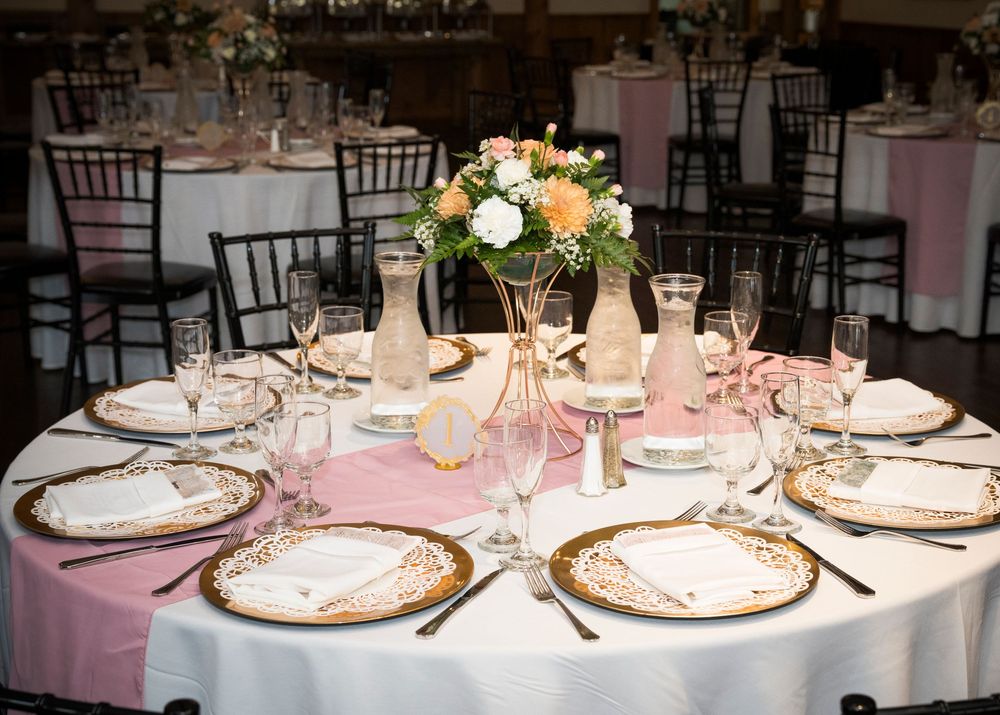 Elegant wedding reception tables decorated with white linens, floral centerpieces, and formal place settings in a banquet hall.