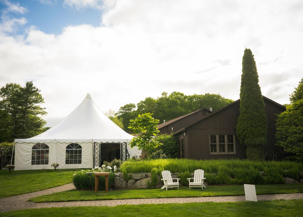 White event tent and Adirondack chairs set up on a landscaped lawn next to a building on a sunny summer day.