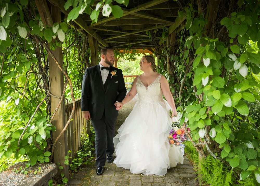 Wedding couple poses for romantic photos under lush green garden archways and foliage.