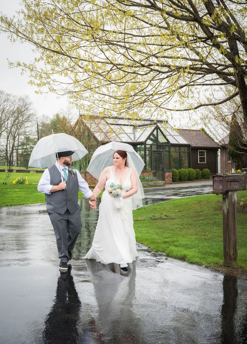 A couple shares a romantic moment under umbrellas on a rainy spring day during their outdoor wedding photoshoot.