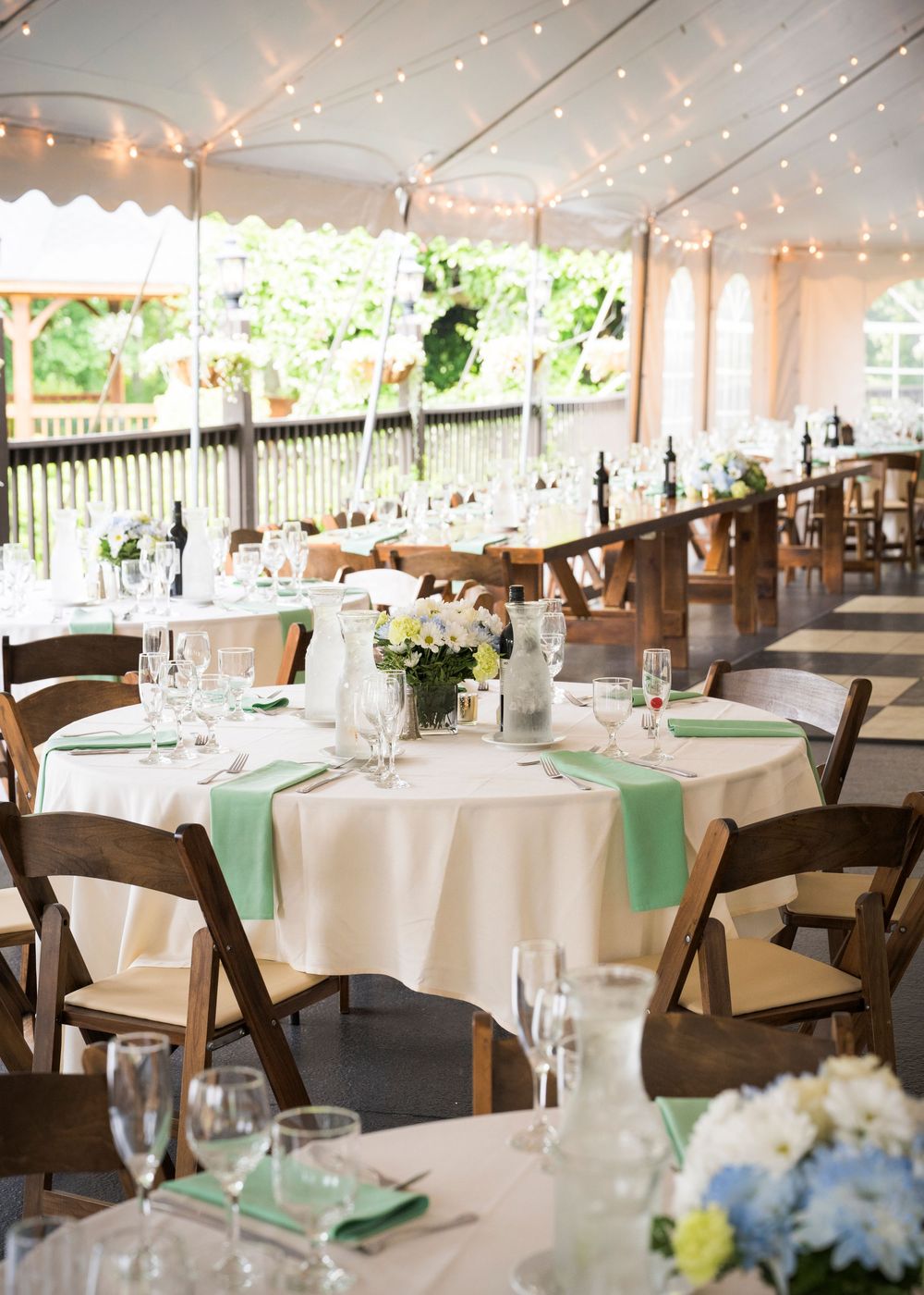 Wedding reception venue with white tables, wooden chairs, and string lights under an elegant white tent.