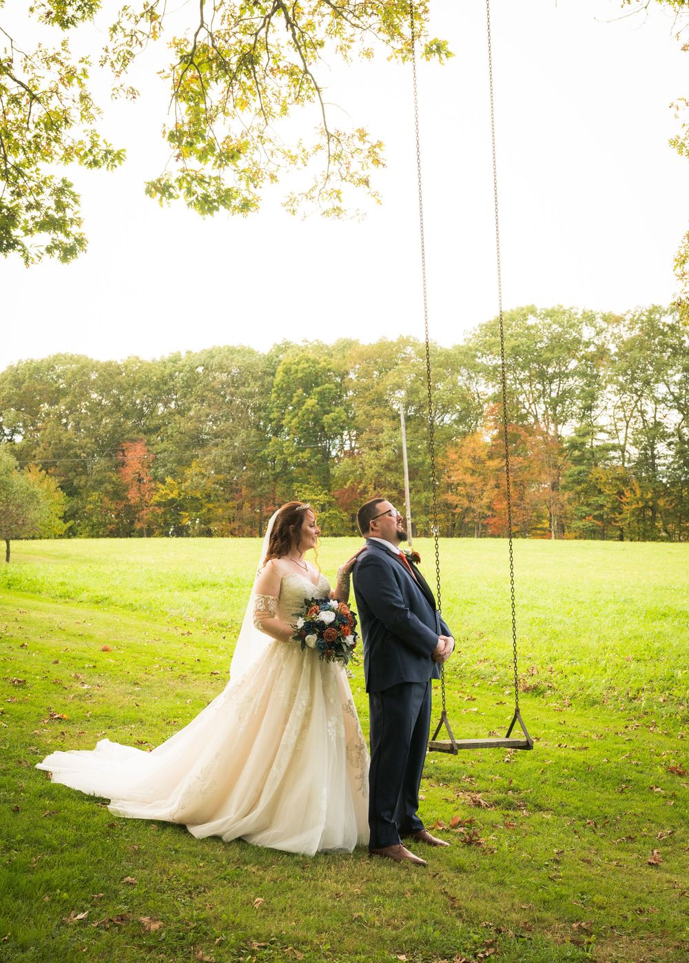 A couple shares a romantic moment on a wooden swing in a scenic autumn hillside setting.