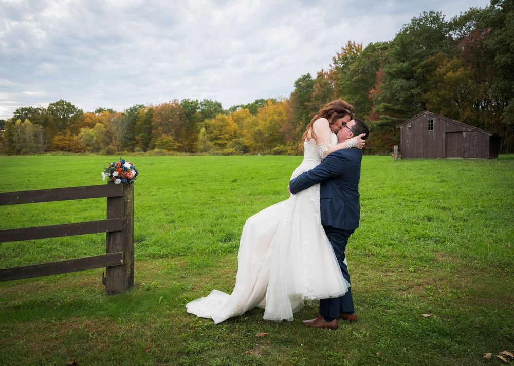 Newlyweds enjoy candid moments together in a rustic farm setting with wooden fences.