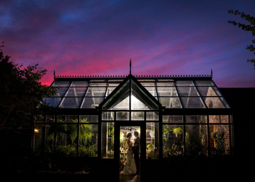 Glass conservatory venue silhouetted against dramatic purple and pink sunset sky.