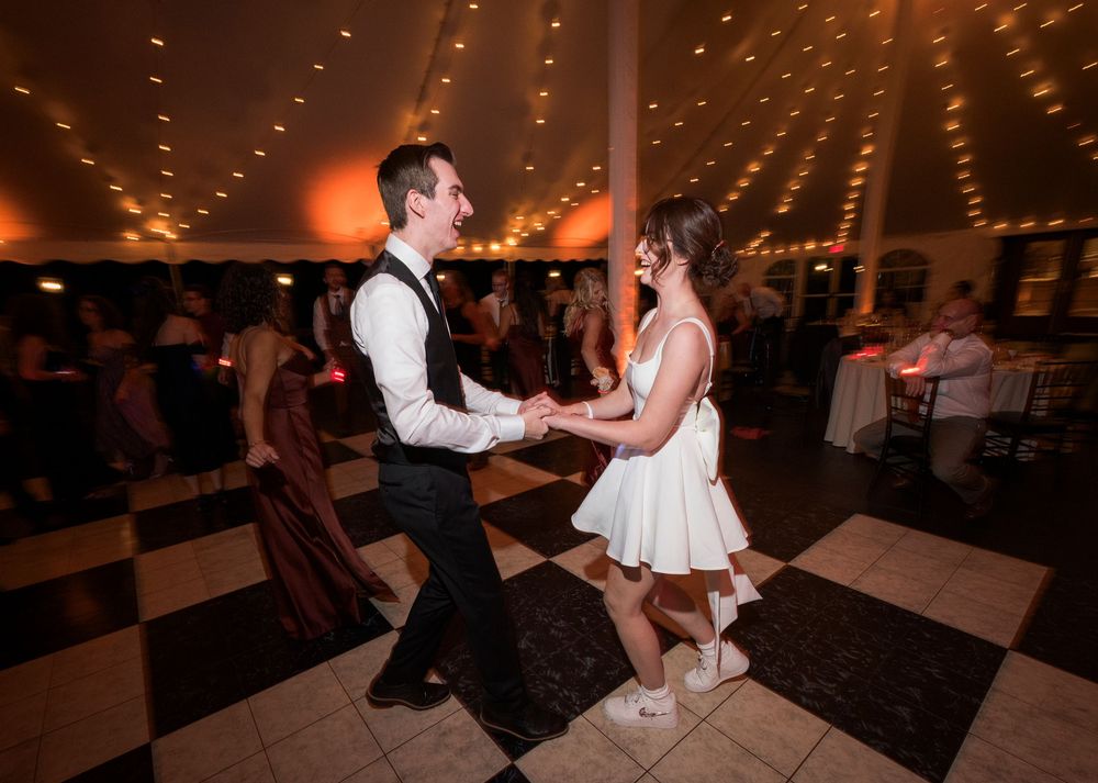 A couple dances on a checkered floor under twinkling lights at a wedding reception.