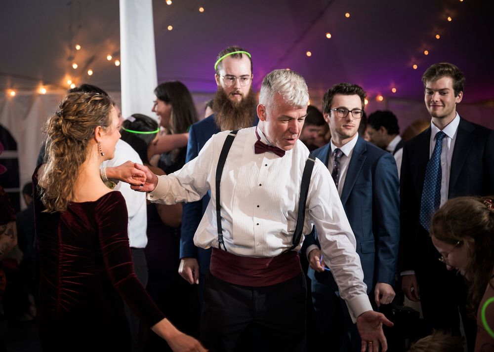 Wedding guests dancing and celebrating at an evening reception with ambient lighting and festive atmosphere.
