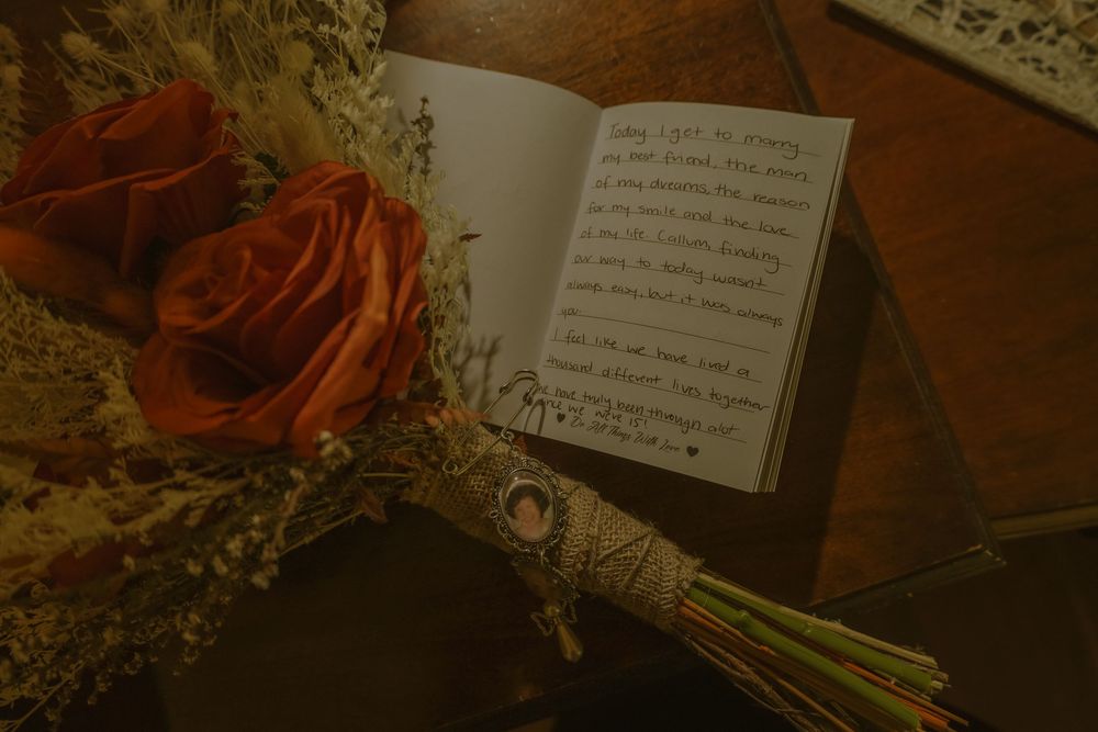A handwritten note lies beside red roses and dried flowers in a vintage-style romantic composition.