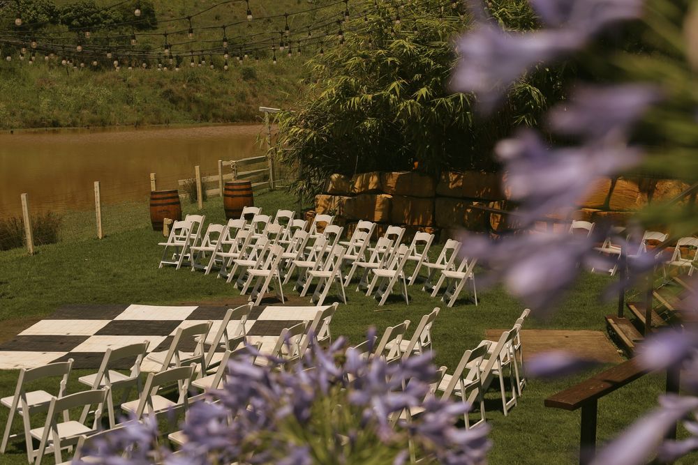 White folding chairs arranged in rows for an outdoor wedding ceremony with purple flowers in the foreground.