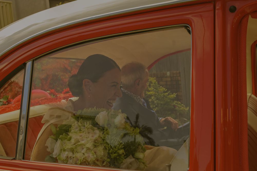 Two people sit in a vintage red car with soft lighting visible through the window.