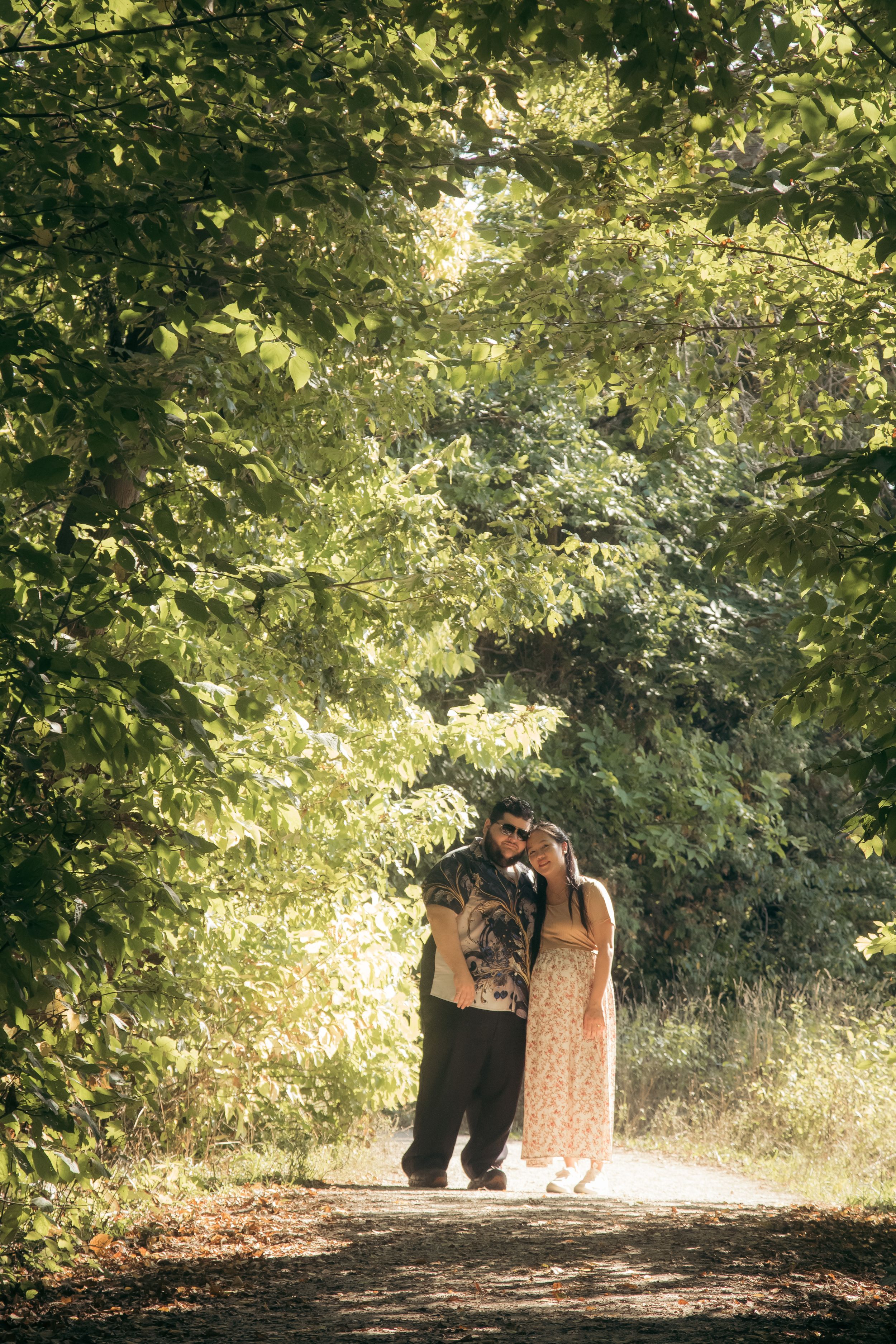 A couple walks down a sunlit tree-lined path on a romantic autumn afternoon.